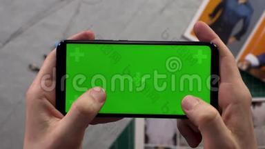 男人的特写镜头`双手拿着智能手机，背景衣柜里有一个水平的绿色屏幕，准备着衣服